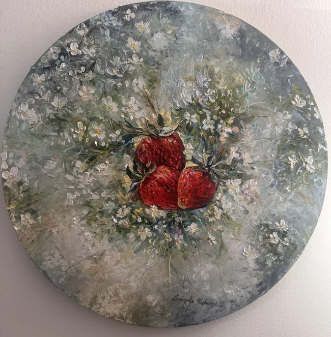 Three red strawberries sit at the centre of a round composition, surrounded by small white flowers, delicate stems, and a softly textured grey-green field.