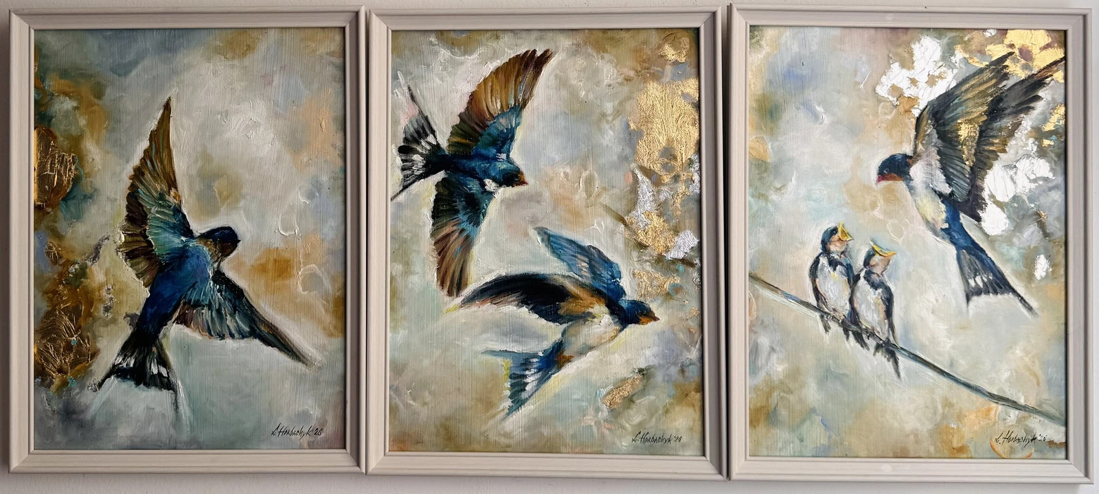 A coordinated set of three panels follows swallows in flight and at rest. Deep blue wings move across soft grey, cream and ochre backgrounds, while bright metallic-looking accents and raised brushwork connect the airborne birds with a pair of nestlings perched on a branch.